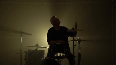 Karanlık bir stüdyoda, dumanlı ve neon ışıklı davul setinde davul çalan siluet davulcusu. Performans vokali ve müzik grubu. Yakın plan..