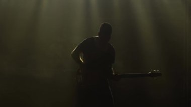 Karanlık bir stüdyoda, dumanlı ve neon ışıklı sahnede elektro gitarda çalan genç bir adamın silueti..