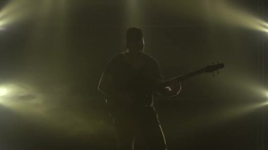 Karanlık bir stüdyoda, dumanlı ve neon ışıklı sahnede elektro gitarda çalan genç bir adamın silueti..