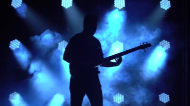 Karanlık bir stüdyoda, dumanlı ve neon ışıklı sahnede elektro gitarda çalan genç bir adamın silueti..