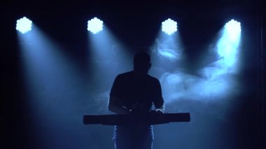 Karanlık stüdyoda, sentezleyici piyano klavyesinde neon ışıkla çalan müzisyen silueti. Neon ışık efektleri. Performans vokal ve müzik grubu.