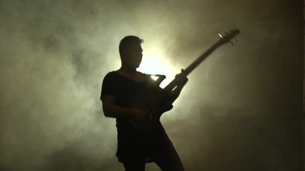 Sylwetka młodego faceta grającego na gitarze elektrycznej na scenie w ciemnym studio z dymem i neonowym oświetleniem. — Wideo stockowe