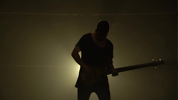 연기와 네온 조명이 있는 어두운 스튜디오에서 무대에서 일렉트릭 기타로 연주하고 있는 한 젊은 남자의 실루엣. — 비디오