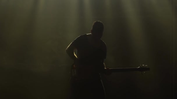 Silhouette d'un jeune homme jouant de la guitare électrique sur scène dans un studio sombre avec de la fumée et un éclairage au néon. — Video