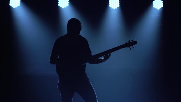 Silhueta de um jovem tocando na guitarra elétrica no palco em um estúdio escuro com fumaça e iluminação de néon . — Vídeo de Stock