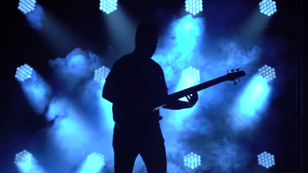 Silhuett av en ung kille som spelar på elgitarr på scen i en mörk studio med rök och neonbelysning. — Stockvideo