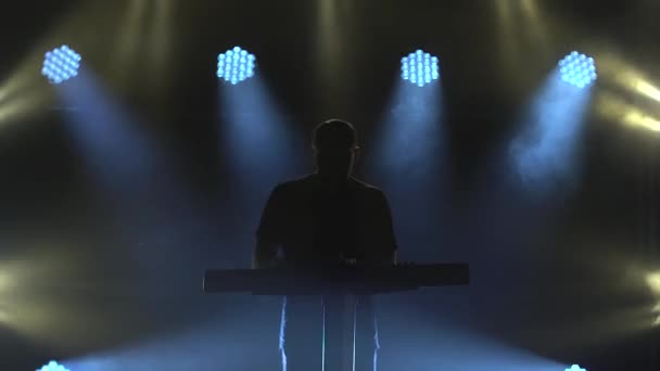 Karanlık stüdyoda, sentezleyici piyano klavyesinde neon ışıkla çalan müzisyen silueti. Dinamik neon ışık efektleri. Performans vokal ve müzik grubu. — Stok video