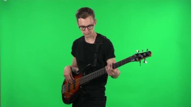 Elektro gitar çalan profesyonel bir müzisyen. Stüdyodaki yeşil ekranda gözlüklü ve siyah tişörtlü genç adam..