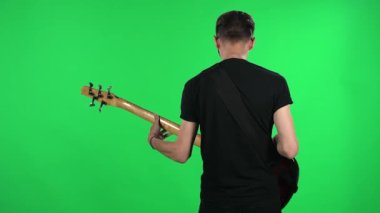 Elektro gitar çalan profesyonel bir müzisyen. Stüdyodaki yeşil ekranda gözlüklü ve siyah tişörtlü genç adam. Arka plan.