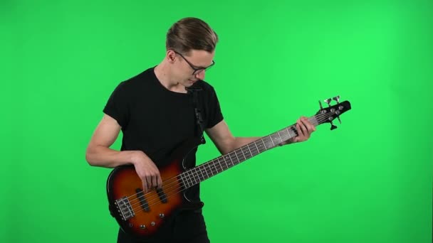 Retrato músico profissional tocando a guitarra elétrica. Jovem com óculos e uma camiseta preta em uma tela verde no estúdio . — Vídeo de Stock