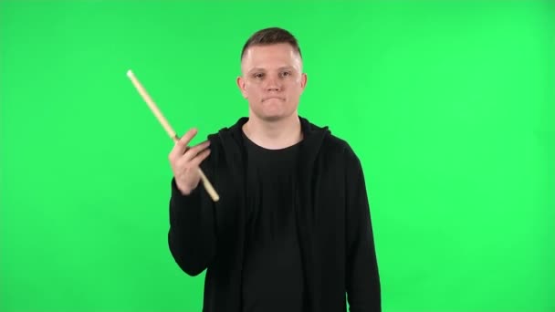 Portret perkusisty obracającego pałeczki perkusyjne. Młody facet w czarnej kurtce na zielonym ekranie w studio. — Wideo stockowe