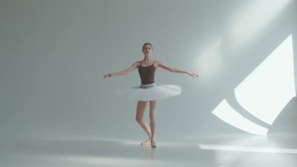 Молода балерина у взутті та білий балет роблять піруети. знімок на білому тлі в просторій і яскраво освітленій студії . — стокове відео