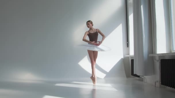 Bailarina joven entrenando en el estudio de pie junto a la ventana. Chica flexible sobre un fondo blanco en luz brillante. — Vídeos de Stock