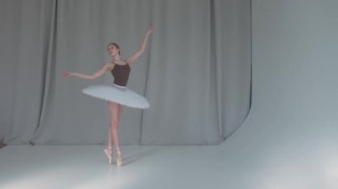 Genç, gelecek vaat eden bir balerin klasik bir bale dansı yapıyor. Beyaz arka plan ve parlak ışıklandırma stüdyoda.