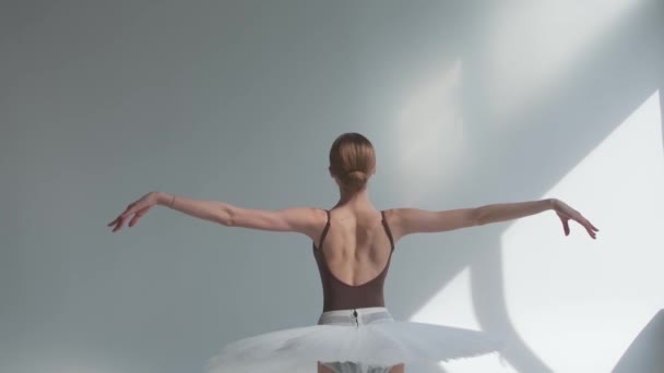 Ballerina op een witte achtergrond die met haar rug staat voert gladde bewegingen uit met haar handen. Gracieuze repetitie van het deel van de witte zwaan in een ruime hal. Sluiten.. — Stockvideo