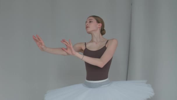 Bailarina em um fundo de cor clara executa movimentos suaves com as mãos. Ensaio gracioso da parte do cisne branco em um salão espaçoso. Fechar. — Vídeo de Stock