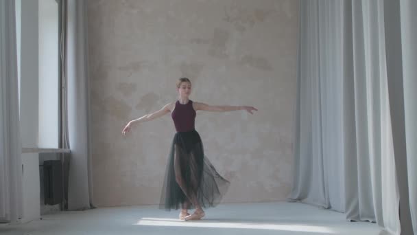 Giovane ballerina in una gonna nera trasparenteformazione in stile loft studio in piedi vicino alla finestra. Ragazza flessibile su uno sfondo parete leggera in luce intensa. — Video Stock