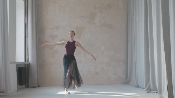 Bailarina flexível em uma saia transparente preta executa um movimento de pirueta pela janela. Estúdio estilo loft com luz do dia brilhante e longas cortinas. — Vídeo de Stock