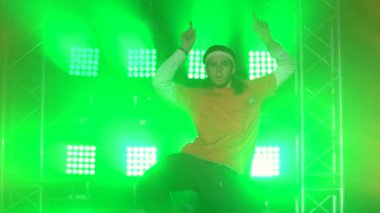 Karanlık stüdyoda tek başına dans eden modaya uygun genç adam, neon ışığı, bir sürü duman. Breakdance konsepti. Moda sokak kıyafeti. Siluet. Kapat..