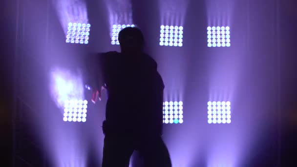 Black silhouette against the background of purple spotlights in a dark studio. Young energetic guy dancing hip hop, freestyle, street dance. Close up. — Stock Video