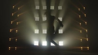 Karanlık stüdyoda hip-hop dansı yapan çekici bir adam, neon ışığı, bolca duman. Modern dans gösterisi yapan şık kıyafetli şirin bir adamın silueti. Ritmi hisset..