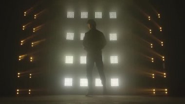 Karanlık stüdyoda hip-hop dansı yapan çekici bir adam, neon ışığı, bolca duman. Modern dans gösterisi yapan şık kıyafetli şirin bir adamın silueti. Ritmi hisset..