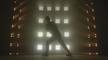 Karanlık stüdyoda hip-hop dansı yapan çekici bir adam, neon ışığı, bolca duman. Modern dans gösterisi yapan şık kıyafetli şirin bir adamın silueti. Ritmi hisset..