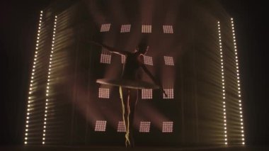 Stüdyoda siyah arka planda beyaz elbiseyle dans eden zarif, çalışkan bir balerin. Çalışkan bale dansçısı klasik bale öğeleri söylüyor..