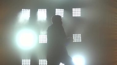 Genç adam break dans, hip hop, stüdyoda sokak dansı, izole edilmiş. Sahne ışıkları önünde şık bir adamın koyu bir silueti. Kapatın. Yavaş çekim.