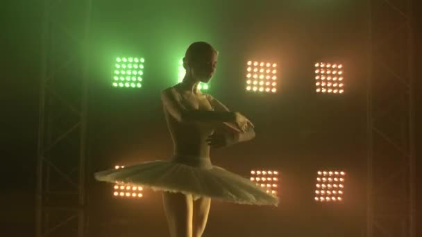 专业芭蕾舞演员在聚光灯下跳芭蕾舞,在大舞台上抽烟.在泛光灯的衬托下，一个身穿白色燕尾服的年轻漂亮姑娘的瘦长轮廓。靠近点. — 图库视频影像