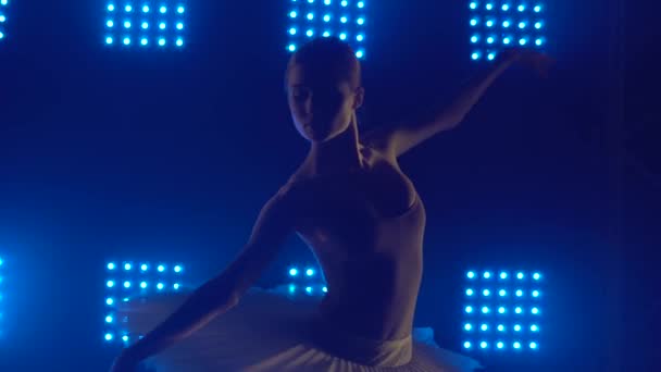 Silhouette schöne junge Ballerina in der Dunkelheit. Balletttraining. Dunkles Studio mit blauem Rauch und Neonlicht. Dynamische Lichteffekte. Nahaufnahme. — Stockvideo