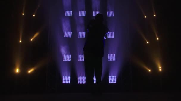Silhouette av en trendy ung hiphop danser i en beskyttende medisinsk maske. Hip hop-dans på en scene i et mørkt studio med røyk og neonlys. Frisk og aktiv livsstil. – stockvideo