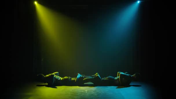 Silhouettes of two male gymnasts doing push-ups and handstands. Well-coordinated teamwork. In the rays of yellow-blue spotlights. Slow motion. — Stock Video