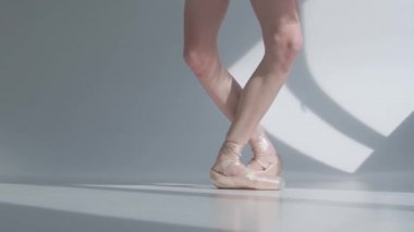 Parmak uçlarında dans eden genç balerin, ayaklar sivri uçlu beyaz arka planda kurdelelerle bağlanmış. Yavaş çekim.