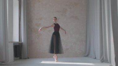 Siyah şeffaf bir etek yağmuru içinde genç bir balerin. Stüdyo dairesi tarzında pencerede duruyor. Işık duvarındaki esnek kız parlak ışıkta. Yavaş çekim.