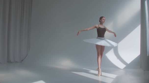 Dançarina faz exercícios de balé em vestido de palco com costas abertas. Ensaios movimentos de dança no estúdio espaçoso banhado pela luz solar. Movimento lento. — Vídeo de Stock