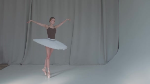 Een jonge veelbelovende ballerina danst een klassiek ballet. Opgenomen in een ruime, helder verlichte studio met gordijnen op de achtergrond. Langzame beweging. — Stockvideo