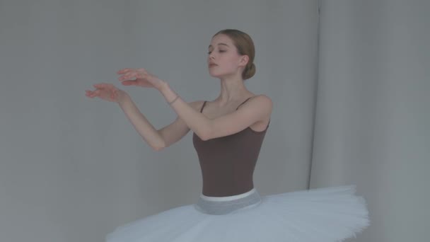 Γυναικείο μπαλέτο σε ανοιχτόχρωμο φόντο εκτελεί απαλές κινήσεις με τα χέρια της. Χαριτωμένη πρόβα του μέρους του λευκού κύκνου σε μια ευρύχωρη αίθουσα. Κλείσε. Αργή κίνηση. — Αρχείο Βίντεο