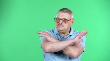 Elleri çapraz olan yaşlı bir adamın portresi. X şekli, inkar anlamına geliyor. Yeşil arka planda izole edilmiş, 