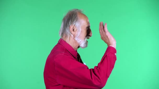 Πορτρέτο του ευτυχισμένος ηλικιωμένος 70s κυματίζει το χέρι και επικοινωνεί με κάποιον, απομονωμένο σε πράσινο φόντο. — Αρχείο Βίντεο