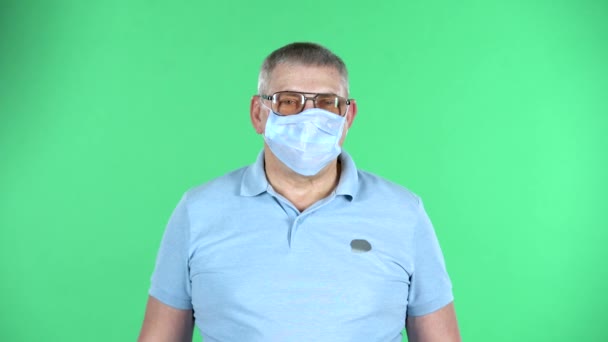 Portrait de l'homme âgé enlève son masque médical jetable et prend une gorge profonde, isolé sur fond vert. — Video