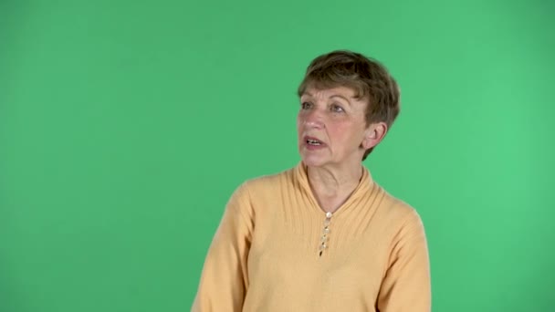 Portræt af ældre kvinde kommunikerer med nogen og peger på noget med godkendelse isoleret over grøn baggrund. – Stock-video