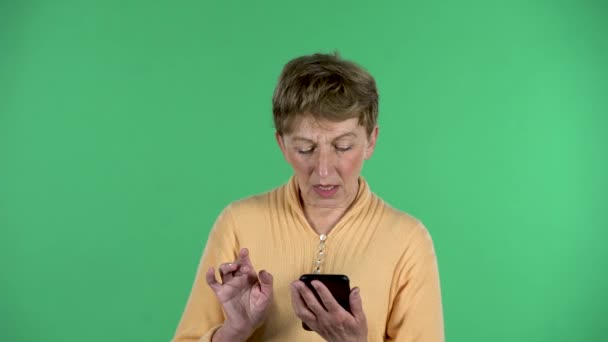 Retrato de mulher idosa está enviando mensagens de texto em seu telefone isolado sobre fundo verde. — Vídeo de Stock