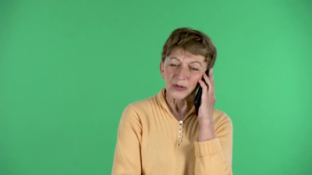 高齢女性の肖像は緑の背景に隔離された携帯電話のために話している. — ストック動画