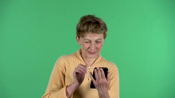 노부인의 모습은 녹색 배경에 격리 된 휴대 전화를 사용하여 비디오 채팅을 하는 모습이다. — 비디오