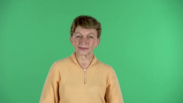 Portret van oudere vrouw is sms 'en op haar telefoon geïsoleerd over groene achtergrond. — Stockvideo