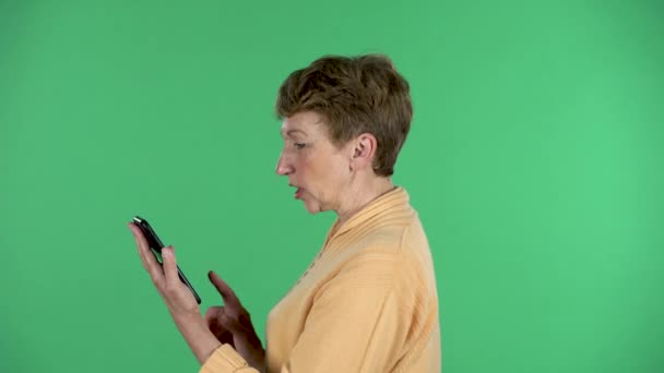 Idős nő beszél video chat segítségével mobiltelefon elszigetelt zöld háttér. Profil nézet — Stock videók