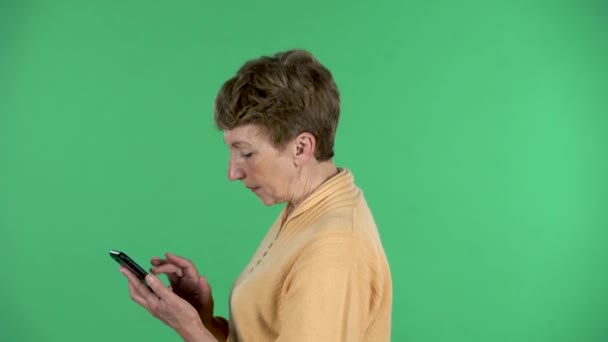 A idosa está a enviar mensagens no telemóvel, isolada por causa do fundo verde. Vista do perfil — Vídeo de Stock