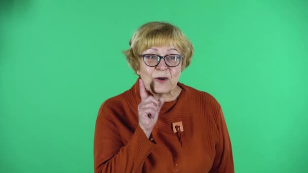 Portrait of senior woman covers her mouth with her hand and whispers the secret and making a hush gesture isolated over green background. — Stock Video