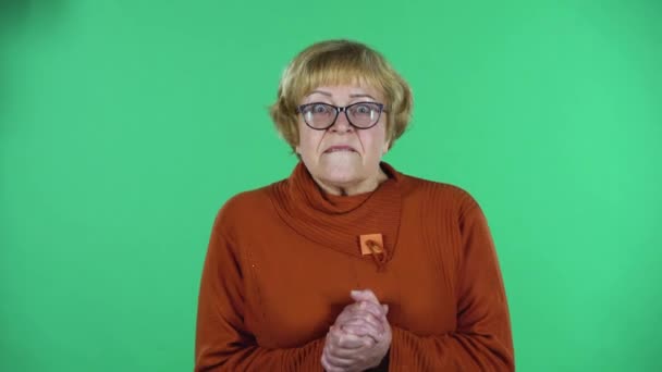 Портрет старшої жінки ретельно досліджує щось, потім боїться дивитися прямо ізольовано на зеленому тлі . — стокове відео